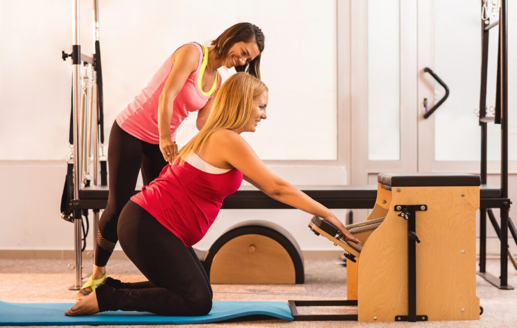 Pilates instructor helping her pregnant client during Pilates class