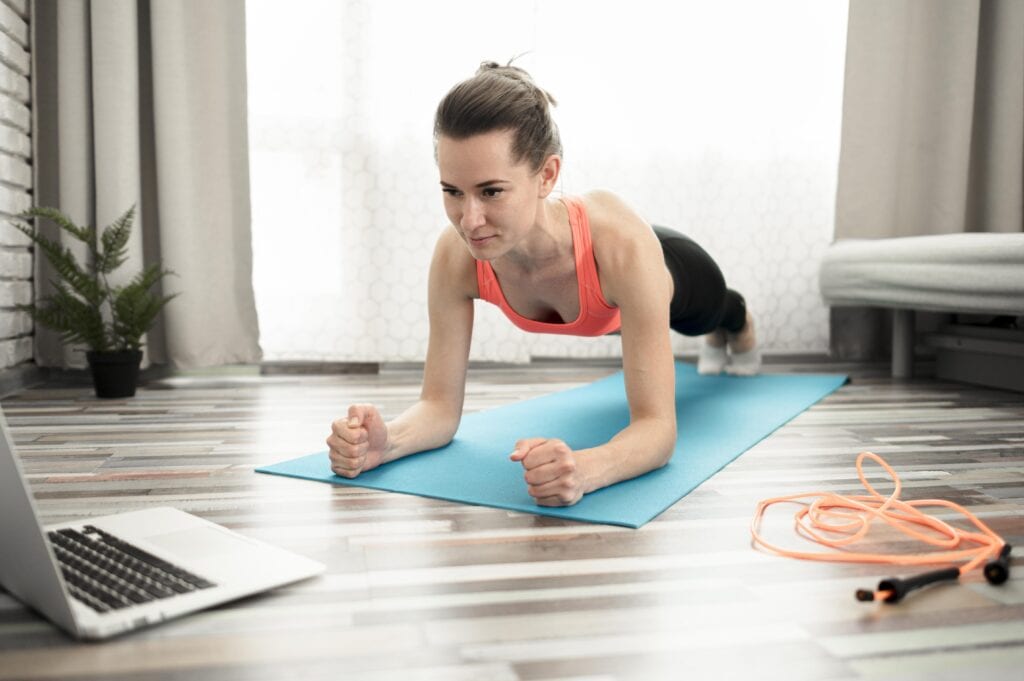 Strong woman doing online workout on mat with jump rope nearby