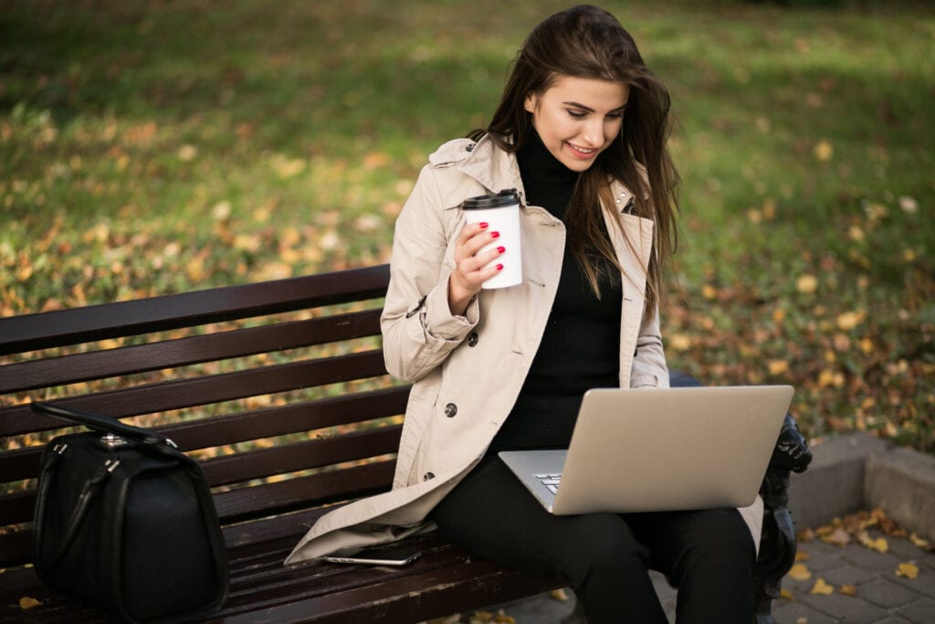 Beautiful woman checking her laptop while drinking coffee at the park