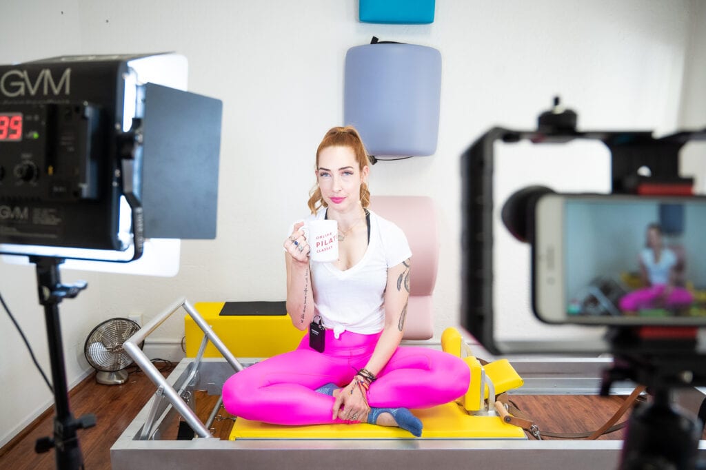 Lesley Logan, Pilates business/studio owner sitting on her Pilates reformer while recording video classes drinking coffee