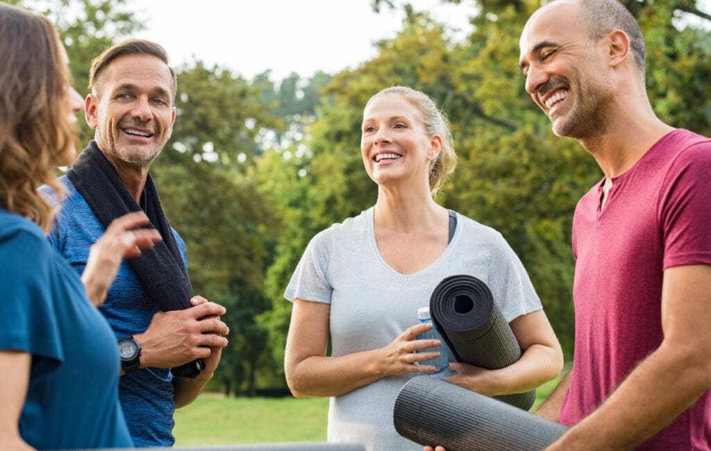Group of adults standing outside talking with yoga mats in hand