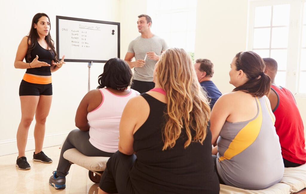 Two coaches reviewing a training plan shown on whiteboard with clients