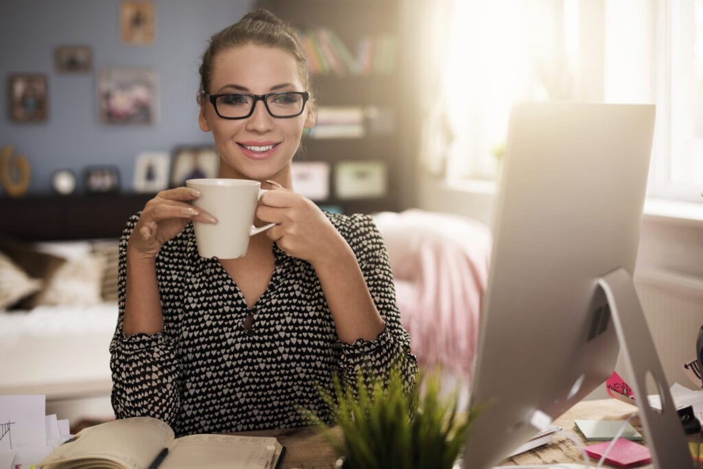 Professional young woman wearing glasses drinking coffee in her home office