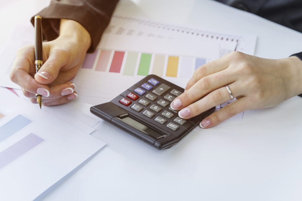 Business owner write down expenses and using a calculator to monitor earnings