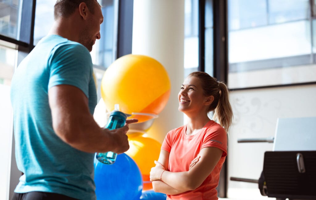 Male and female talking Pilates fitness together in colorful workout clothing.