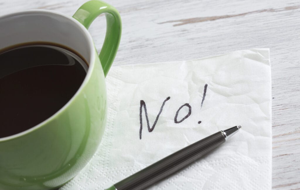 The word "No!" written on tissue paper next to a green mug of coffee