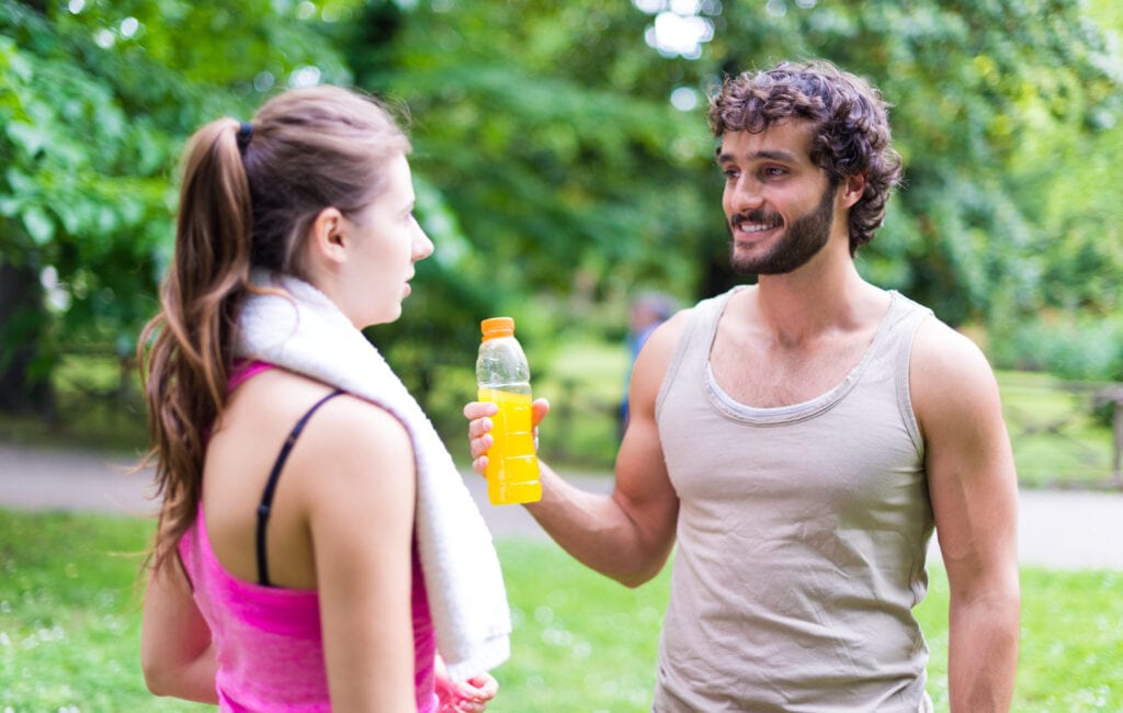 Man holding athletic drink in hand talking to woman in the park after working out
