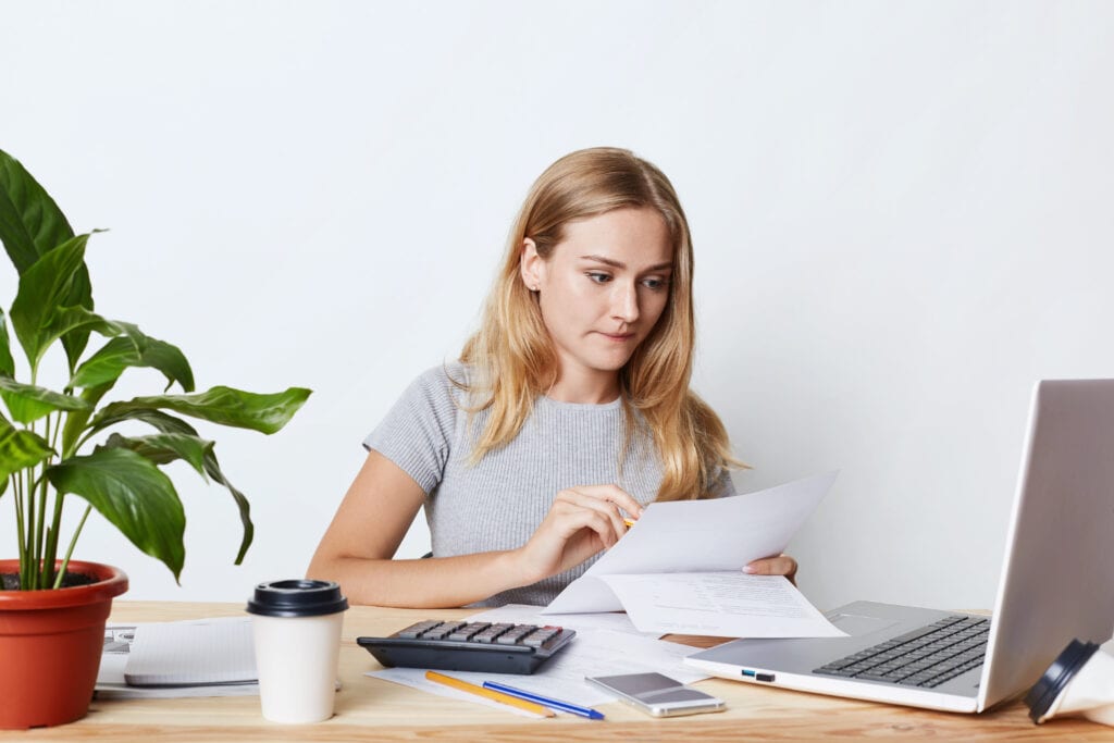 Woman at desk looking at papers computer screen and calculator