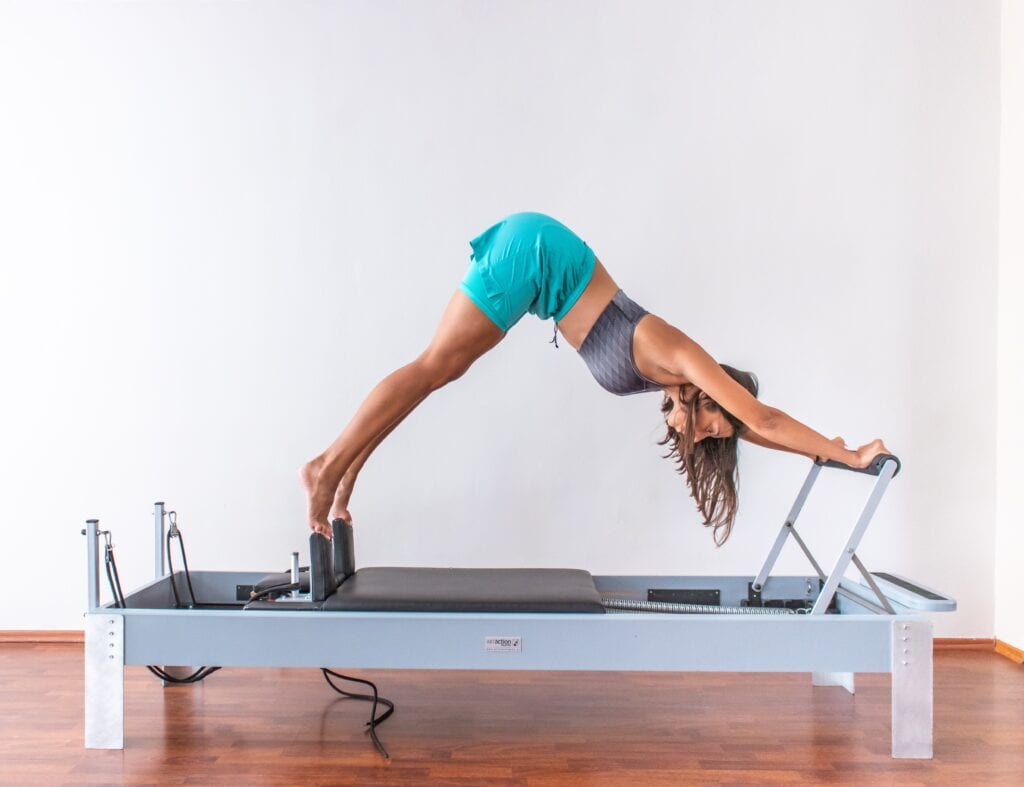 Woman wearing shorts and sports bra exercising in studio on Pilates reformer