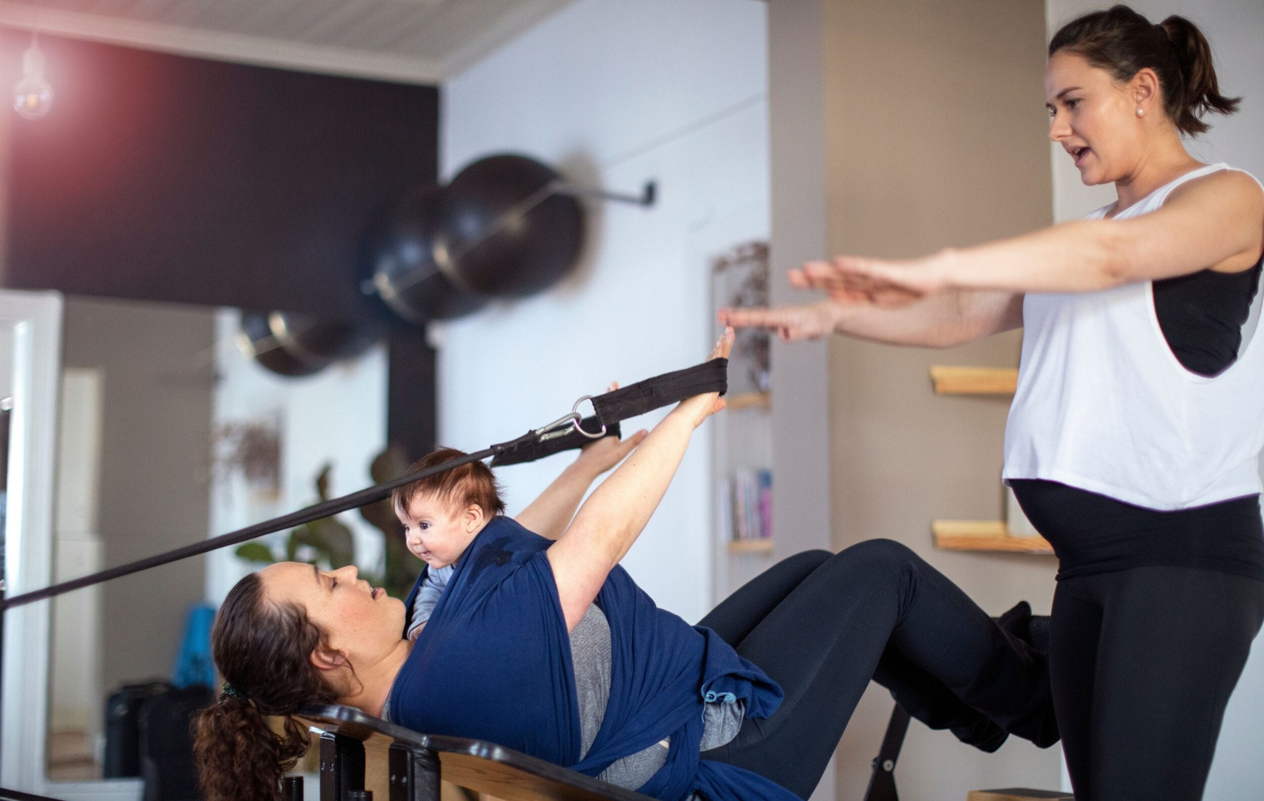 Pregnant Pilates teacher assisting her client while doing the Pilates exercise